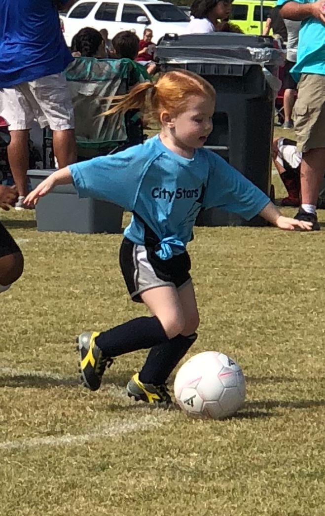 Girl kicking soccer ball along ground