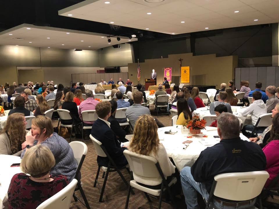 People sit at tables at banquet listening to Mayor Perrin speak.