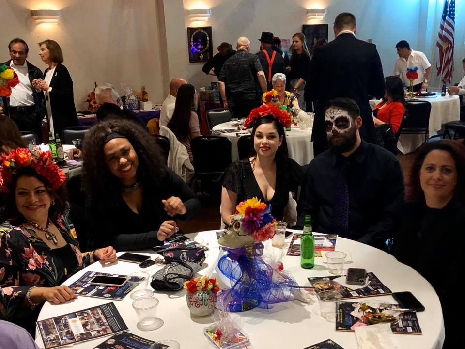 People gathered at table for Dia de Los Muertos, with one wearing face paint of skull