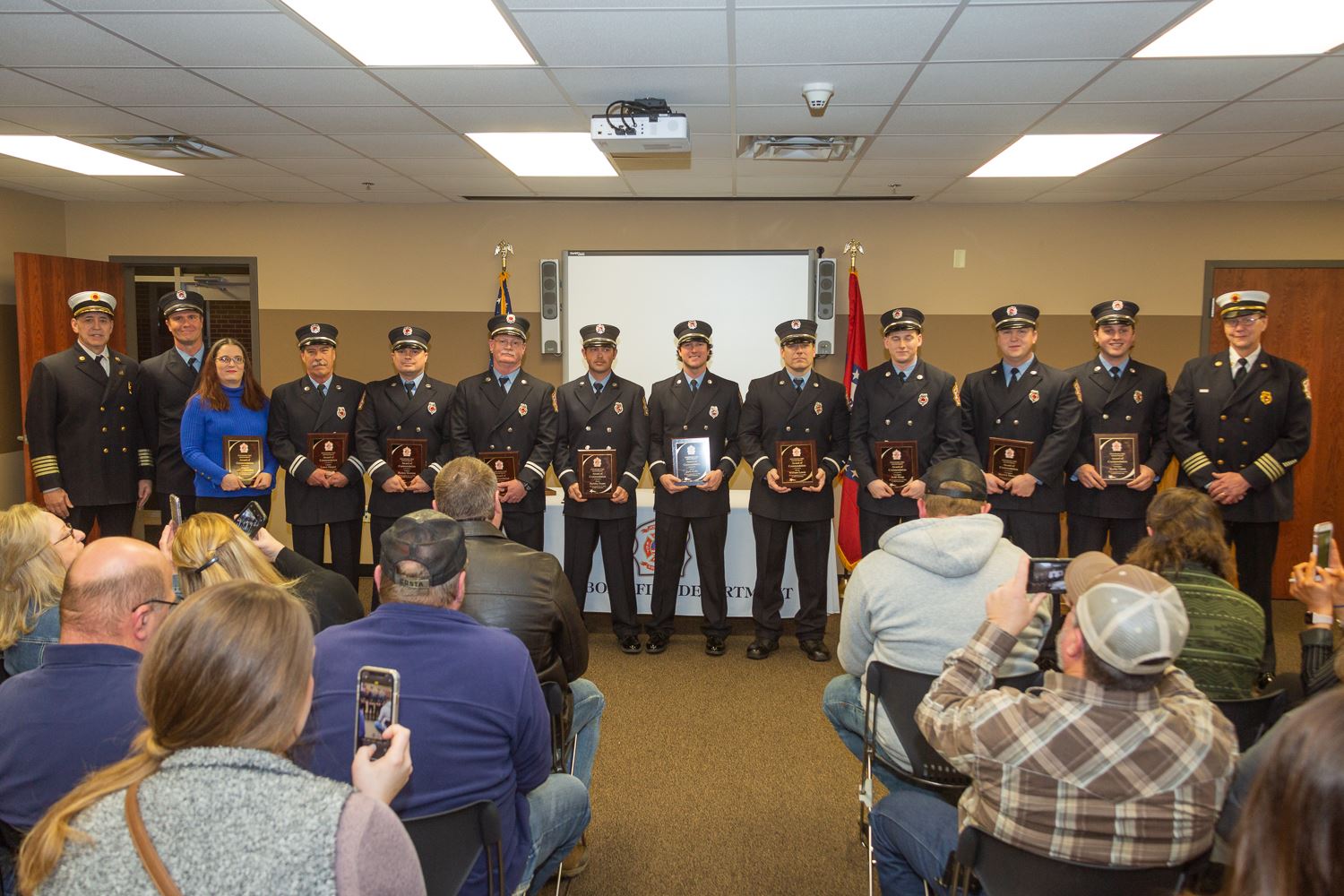 Fire Department Award recipients standing in line in front of audience at awards ceremony holding th