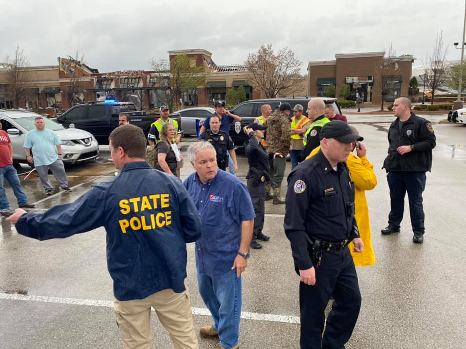 Police at Turtle Creek Mall parking lot with tornado damage behind them to building