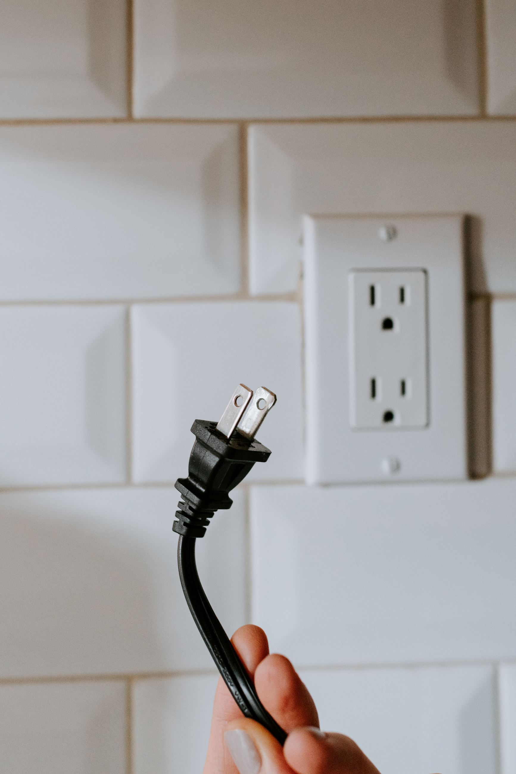hand holding an electrical power cord plug with socket in background