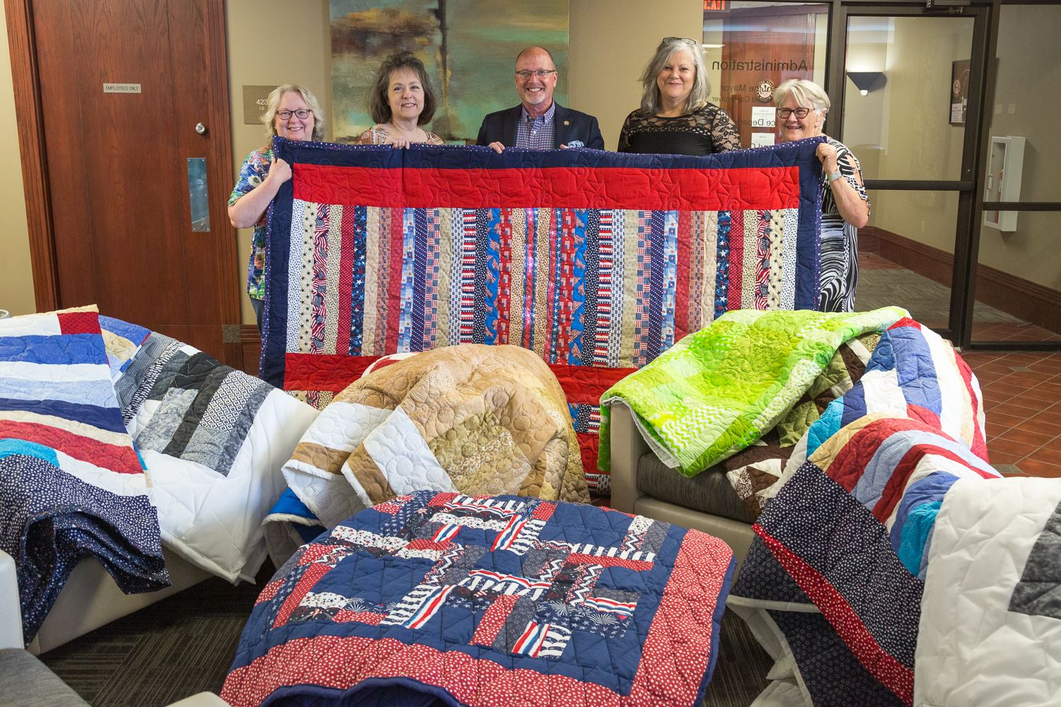 The women and Mayor Copenhaver holding a quilt and surrounded by more quilts all around