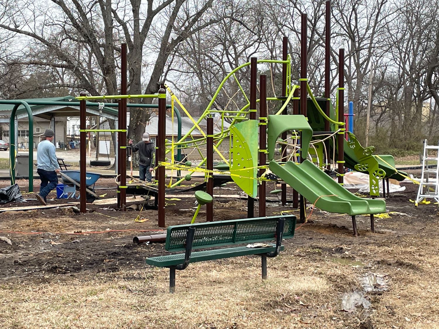 Man with wheelbarrow full of concrete at new large piece of playground equipment