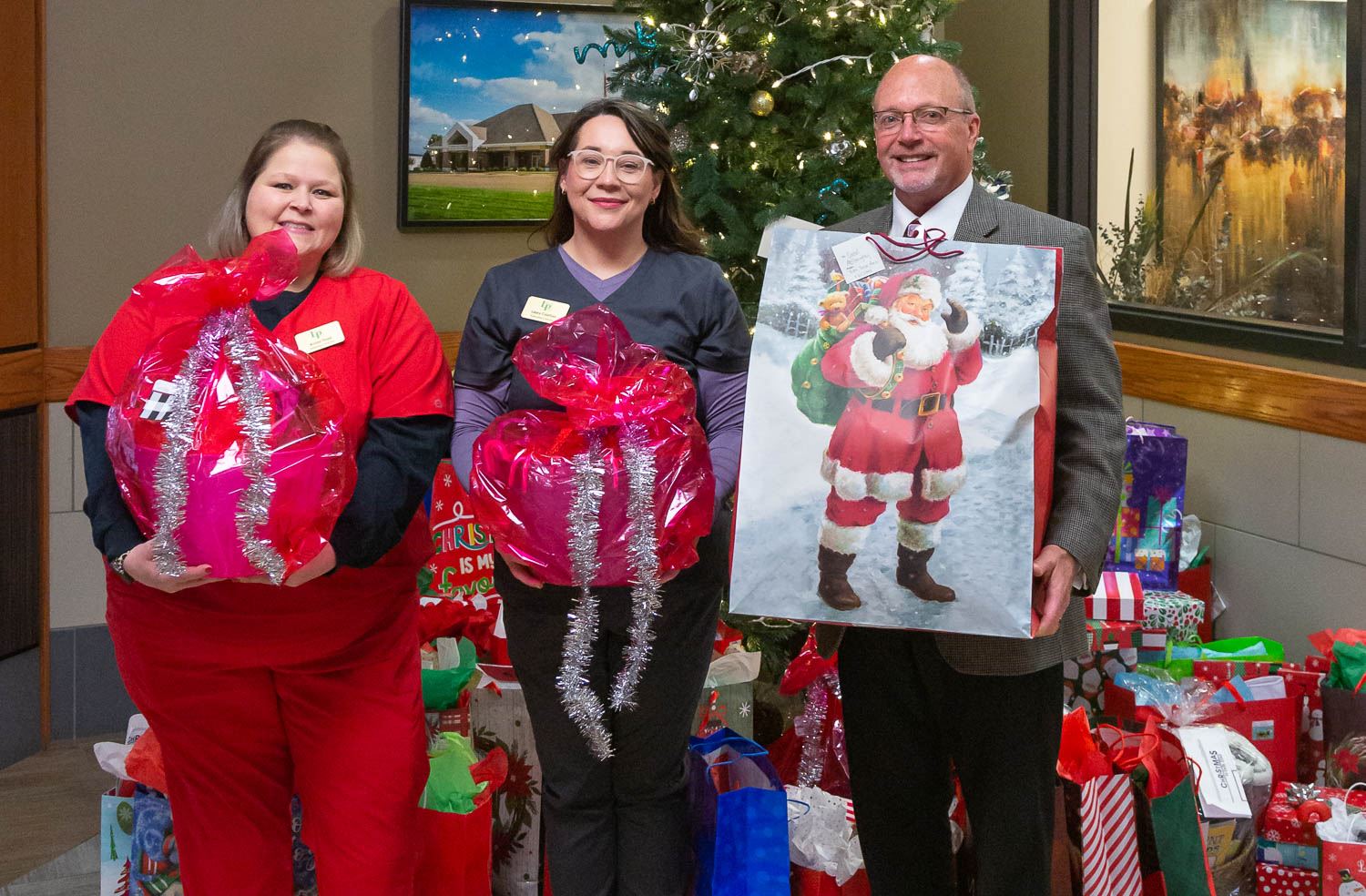 Mayor Copenhaver with Laura Courtois and Krista Floyd holding presents with more underneath the tree
