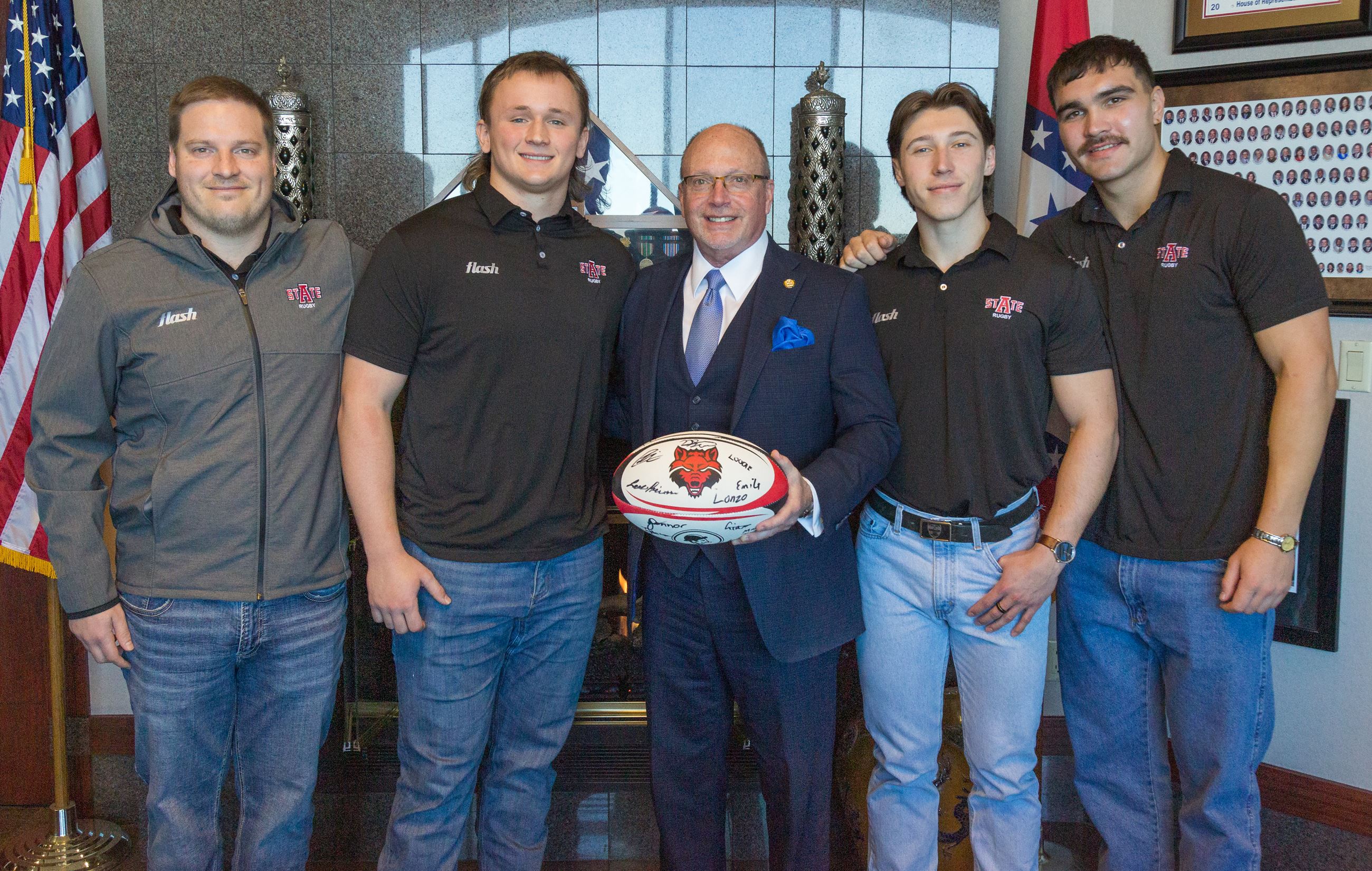 Mayor Copenhaver holding signed rugby ball with coach and team members by his side
