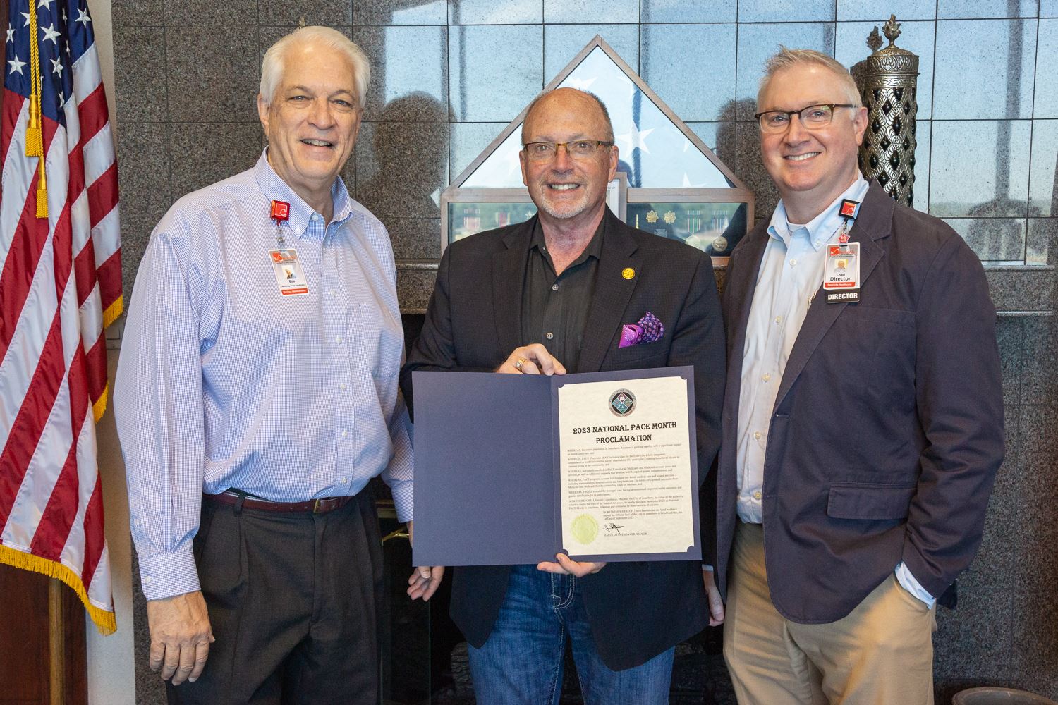 Mayor standing with two of St. Bernards employees and holding proclamation in hand