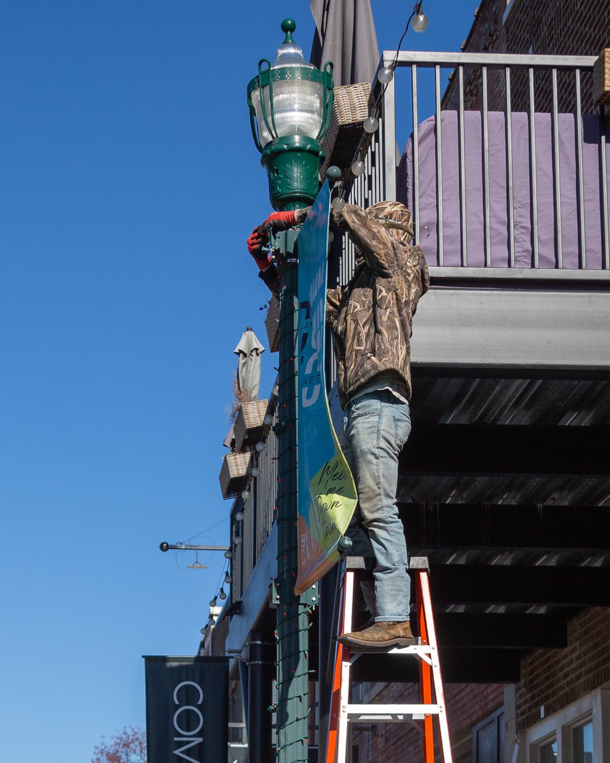 Man on ladder hanging Christmas lights around a light pole